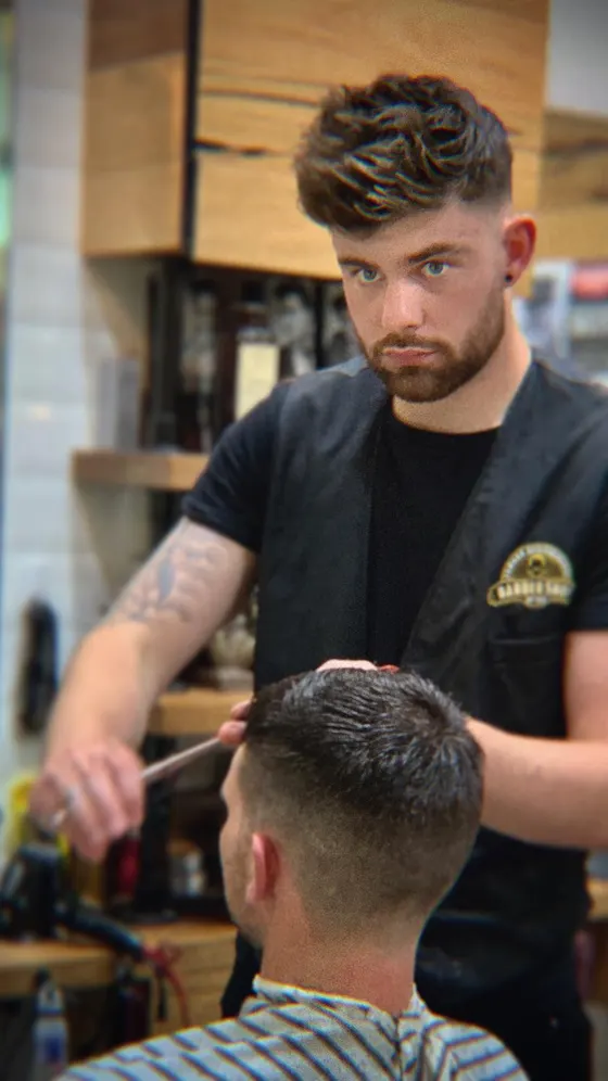 A barber in a shop apron cutting through the top