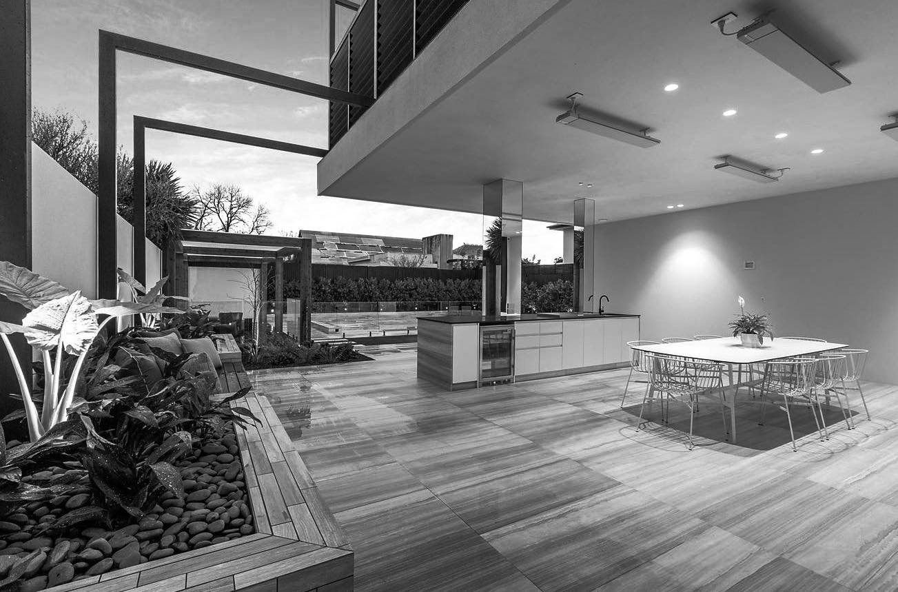 Covered outdoor kitchen and dining area under a deep eave, with built-in joinery and stone benchtops.