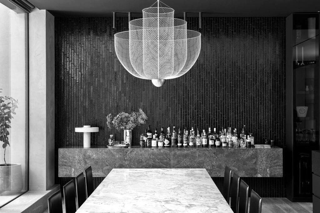 Formal dining room with a stone table, dark fluted timber feature wall and a sculptural glass pendant light above.
