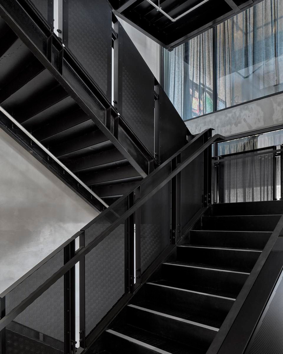 Blackened steel floating staircase beside full-height steel-framed glazing.