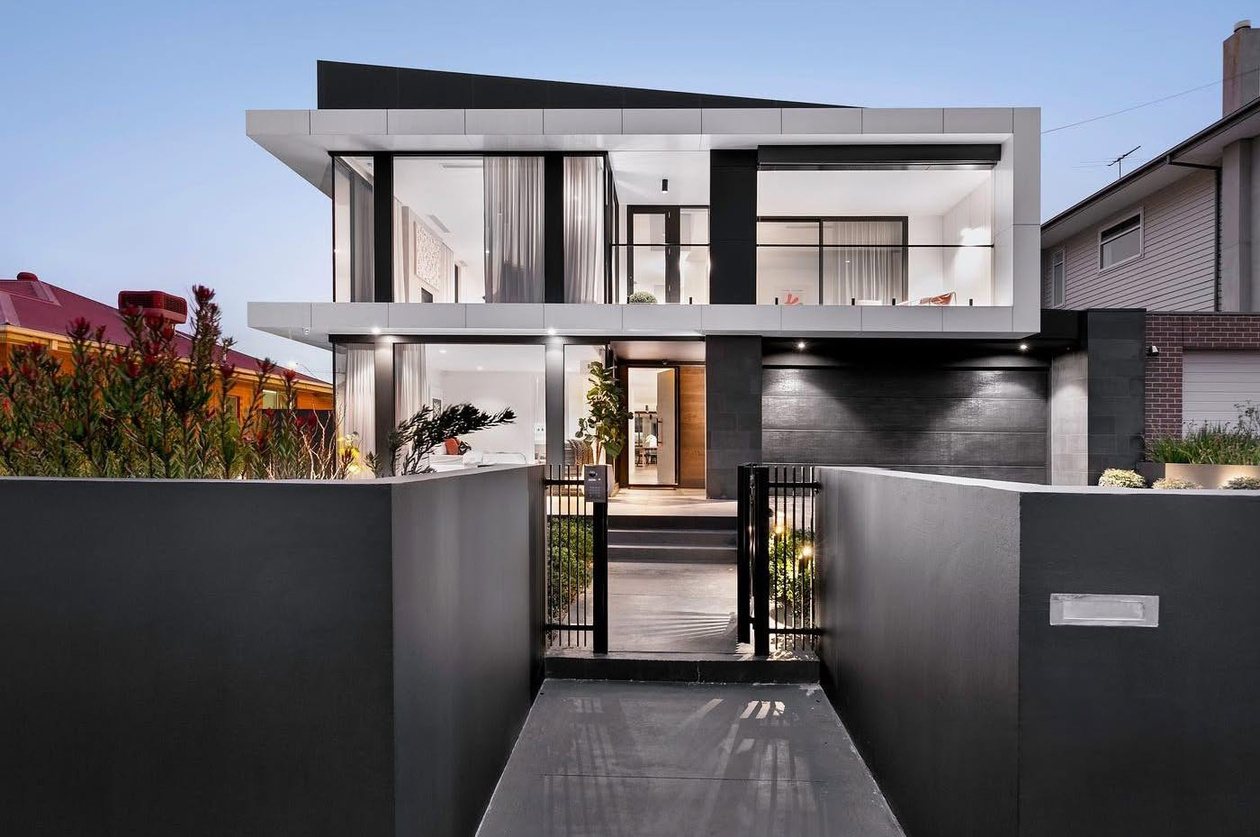 Aberfeldie residence at dusk: contemporary rear extension with charcoal rendered walls, a timber deck and warm interior lighting.