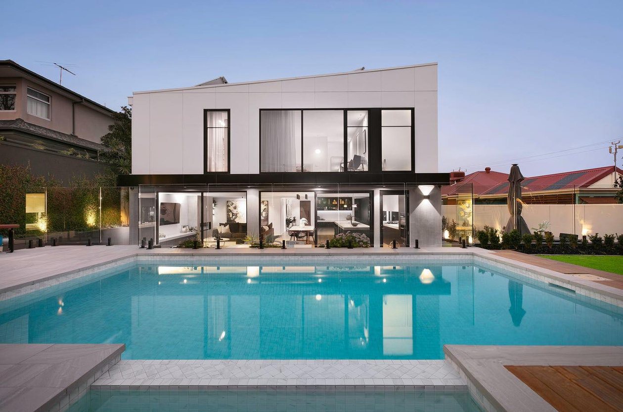Rear garden at dusk with a lap pool reflecting the lit extension, paved surrounds and established planting.