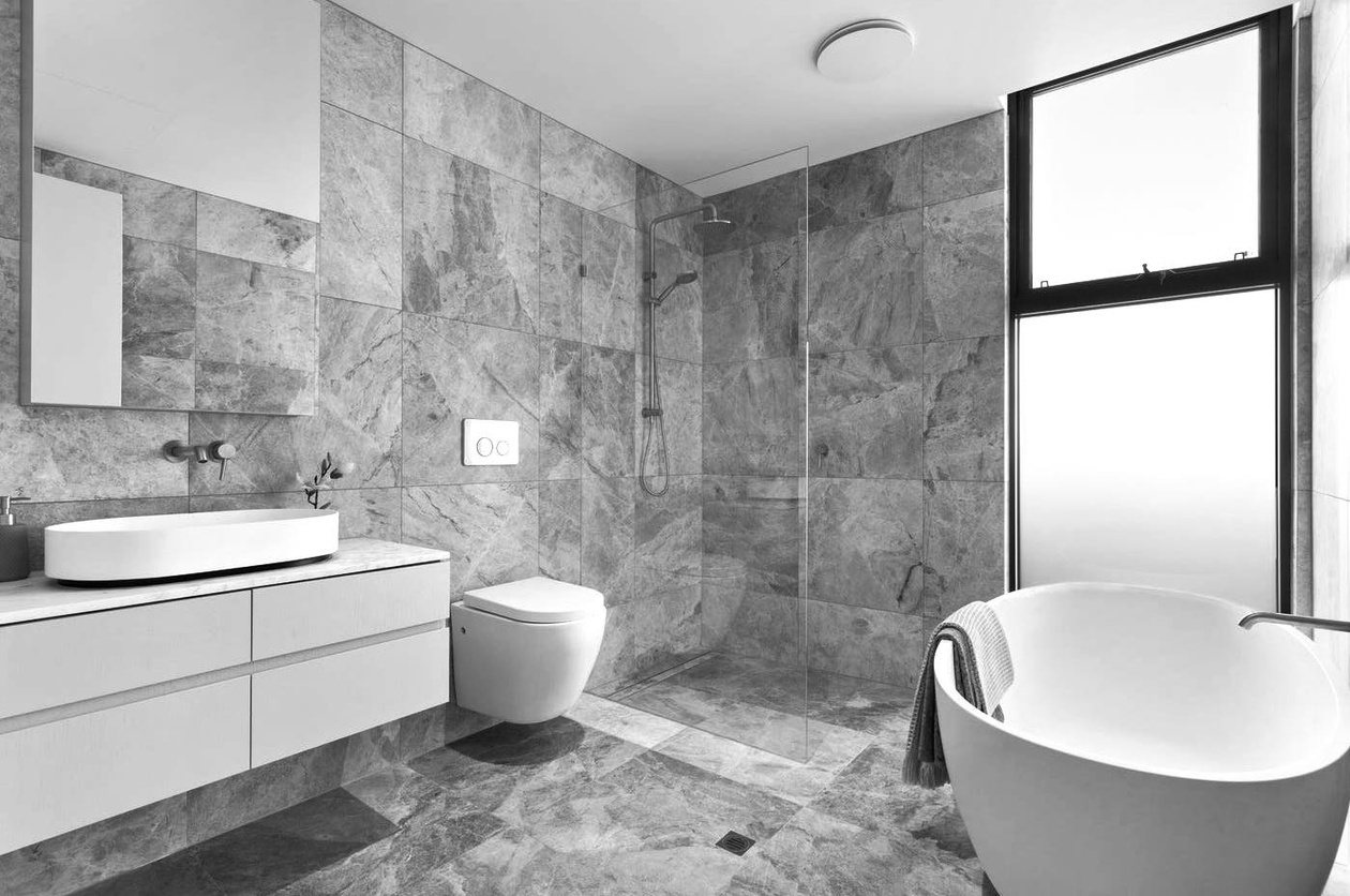 Main bathroom fully lined in grey marble, with a freestanding tub, wall-hung vanity and a slim awning window.