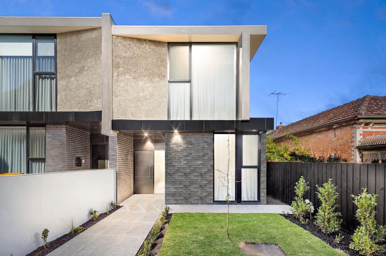 Ascot Vale duplex street façade at dusk with rendered and brick two-storey forms with a recessed entry and warm interior lighting.