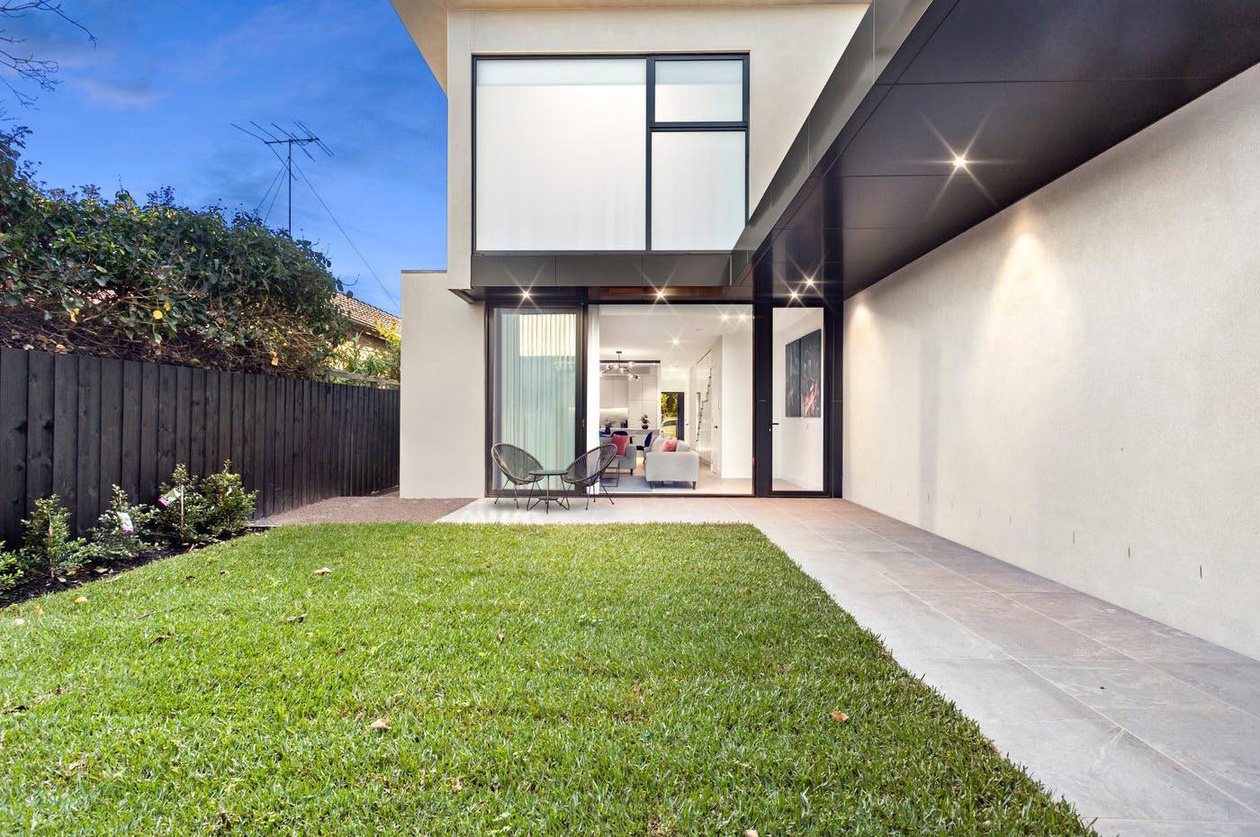 Ascot Vale duplex from the rear lawn at dusk, with a double-height glazed living space glowing against the evening sky.