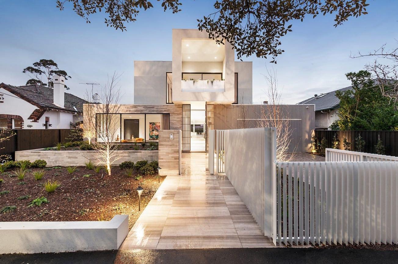 Brighton luxury home at dusk: natural stone and timber-clad façade with a double-height entry and uplit travertine path.