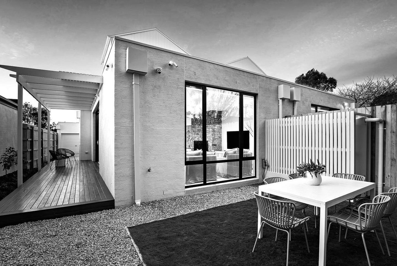 Covered alfresco area with an outdoor dining setting, dark floor tiles and a sliding glass wall connecting it to the living space.