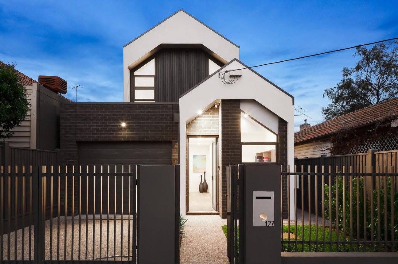 Strathmore custom home at dusk: gabled white and charcoal façade behind a dark vertical batten fence.